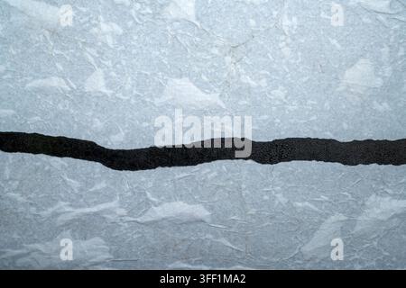 A close-up macro photograph featuring a single, uneven horizontal black glitter strip contrasting against a textured, light gray or silver metallic pa Stock Photo