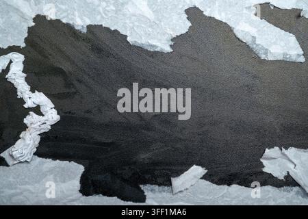 A close-up shot of white paper torn horizontally, revealing a deep black, gritty, and textured background. Concept of mystery, hidden truth, or reveal Stock Photo