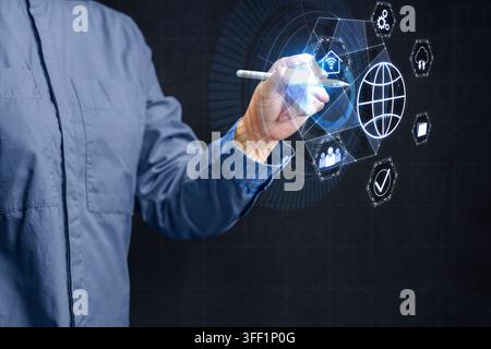 A man in a blue shirt uses a stylus to select icons on a glowing futuristic digital HUD interface displaying global connection, security, and smart ho Stock Photo