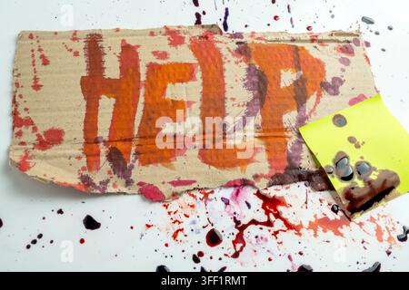 A piece of cardboard with the word HELP painted in red, splattered with dark red blood, and a sticky note on a white background, representing a concep Stock Photo