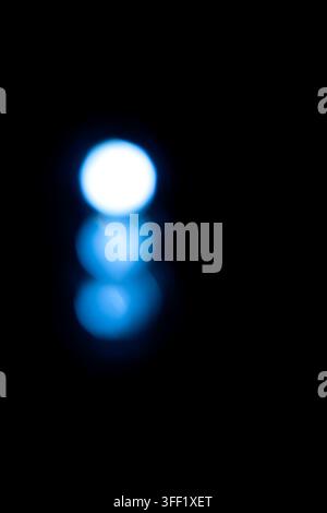 Minimalist abstract image featuring three vertical blue and white bokeh light circles against a solid black background. Abstract blue background Stock Photo