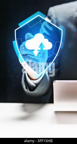 Businessman interacting with a glowing blue digital shield containing a cloud upload and download icon, representing secure cloud storage and data pro Stock Photo
