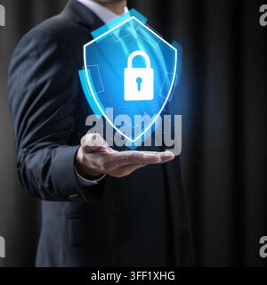 Businessman holding glowing blue digital shield with padlock, representing cybersecurity and data protection. Concept of Digital Protection Stock Photo