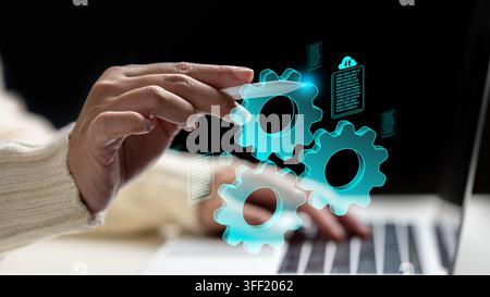 A woman hand using a stylus to interact with glowing blue virtual gears and document icons over a laptop, representing digital automation and workflow Stock Photo