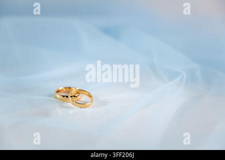 Two gold wedding rings resting on soft white fabric with elegant folds and copy space, symbolizing marriage, love, commitment, partnership and a timel Stock Photo