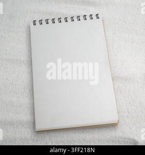 A blank spiral-bound notebook lies open on textured white sand, offering clean copy space for mockups Stock Photo