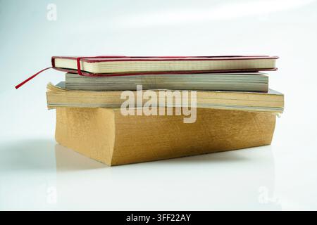 A stack of four different books and notebooks piled on a reflective white surface. Study or education concept Stock Photo