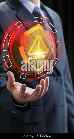 Businessman displaying a glowing orange holographic shield with a malware warning alert, representing cybersecurity threats and data defense. Cybersec Stock Photo