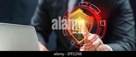 Businessman touching a virtual HUD interface showing a malware warning shield with a laptop nearby. Cybersecurity concept Stock Photo