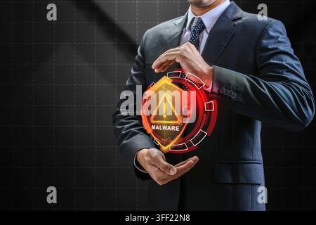 Businessman displaying a glowing orange holographic shield with a malware warning alert, representing cybersecurity threats and data defense. Cybersec Stock Photo