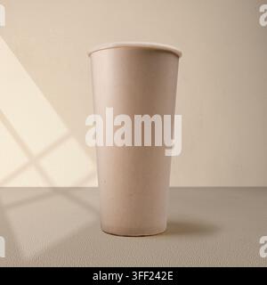 A minimalist mockup of a tall beige paper cup standing on a textured surface with soft window shadow light. Mockup or Copyspace Stock Photo