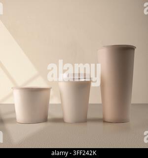 Three blank beige paper cups of different sizes lined up on a neutral surface with soft shadow overlay, perfect for packaging mockup. Mockup or Copysp Stock Photo