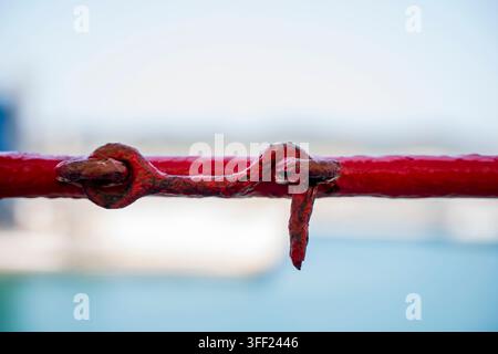 Rusty metal hook and eye latch securing a red painted railing, seen in close up Stock Photo