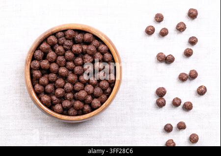 Choco balls, crispy breakfast cereal in a wooden bowl on linen, from above. Crispy corn food made of toasted cornmeal, cocoa powder, and sugar. Photo Stock Photo