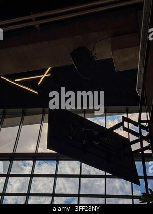 Dramatic view inside a contemporary glass-roofed interior, featuring suspended digital screens, geometric LED lighting and structural elements against Stock Photo