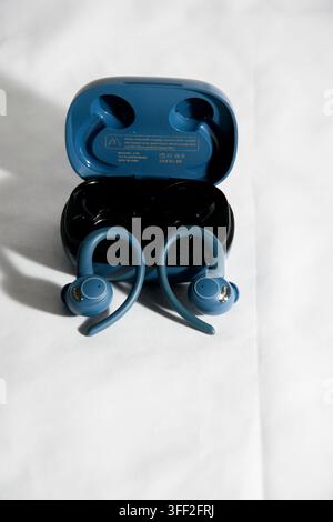 Pair of blue true wireless sports earbuds with open charging case on a white background Stock Photo