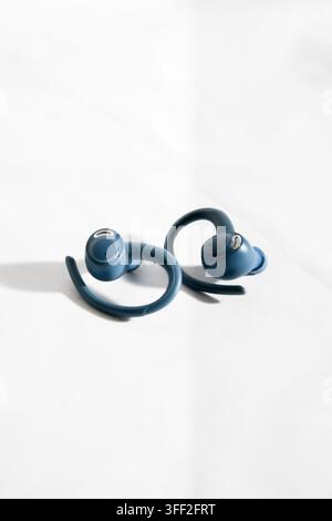 Pair of blue true wireless sports earbuds with ear hooks on a white fabric background Stock Photo