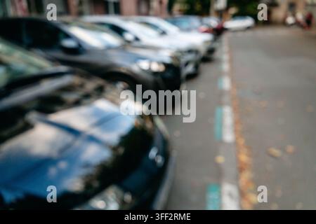 Defocused parked cars line an urban street beside marked parking spaces. The image suits transport parking mobility insurance and city infrastructure Stock Photo