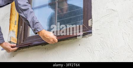 A worker is installing a window sill on a window frame. His hands hold the sill firmly; his movements are precise and neat. The scene illustrates the Stock Photo