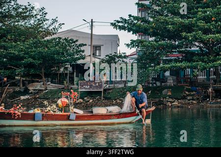 Hoi An, Vietnam - August 27, 2026. A fisherman casts a net from a decorated wooden boat while working on a quiet residential canal. Stock Photo