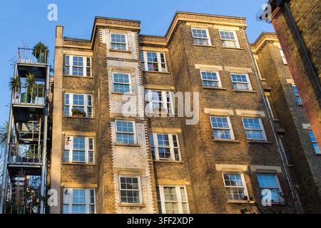 A multi-story brick building in London, England, features a metal fire escape decorated with potted plants to add urban greenery. Stock Photo