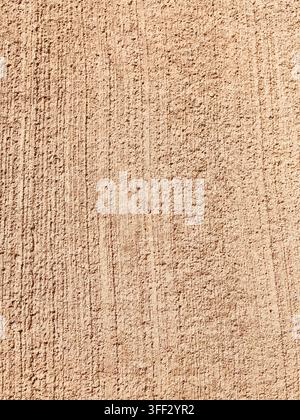 Rough beige stucco wall surface displaying vertical lines and granular texture, suitable for architectural backdrops or abstract design elements Stock Photo