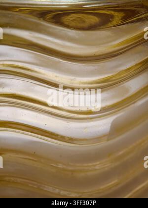 Golden abstract texture showing undulating wavy patterns on a transparent material, creating a dynamic background with reflections and refractions Stock Photo