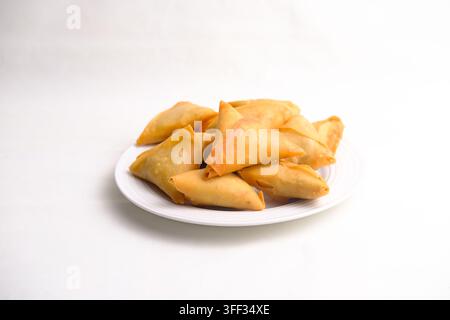 A plate of golden-brown triangular samosas arranged against a clean white background. The crispy fried pastries are presented as a simple food still l Stock Photo