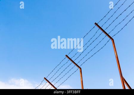 Barbed wire fence posts at prison against blue sky Stock Photo