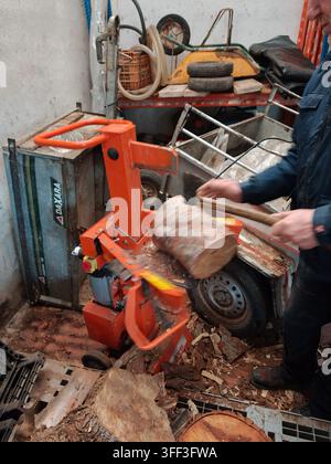 Worker operating a hydraulic log splitter, processing logs into firewood for heating or other uses, creating fuel and preparing for colder seasons in Stock Photo
