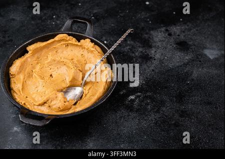 Smooth peanut butter spread in bowl with spoon on dark rustic background. Natural peanut paste made from roasted peanuts Stock Photo