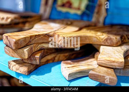 Close-up view of unique handcrafted olive wood cutting boards stacked on a vibrant blue display shelf at a traditional market in Kairouan, Tunisia - 0 Stock Photo