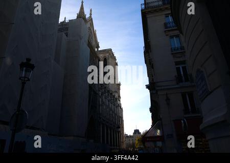 Notre-Dame Cathedral draped in protective restoration scaffolding, framed by classic Parisian buildings under a clear blue sky in Paris, France. Stock Photo