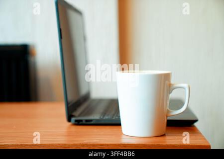 Minimal wooden desk workspace featuring a white coffee mug beside an open laptop. Clean composition with copy space, ideal for remote work, home offic Stock Photo