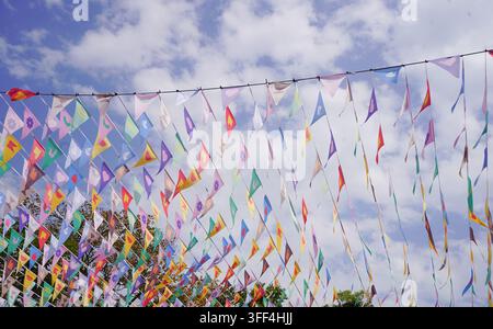 Rows of colorful triangle bunting flags hanging high across the blue sky as outdoor fair decoration. Stock Photo