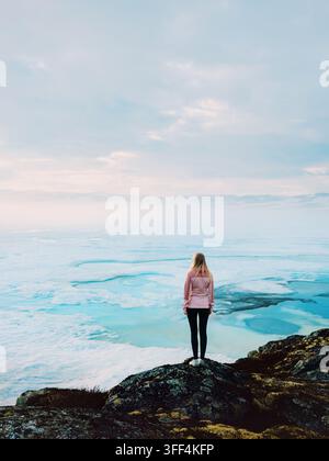 Woman standing alone overlooking frozen lake in Norway quiet winter nature, solo travel adventure outdoor lifestyle solitude contemplation mindfulness Stock Photo