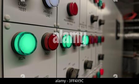 Close-up of an industrial electrical control panel with illuminated green run and red fault indicators, control switches and status lights. Stock Photo