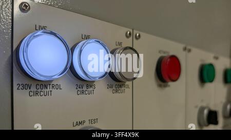 Close-up of an industrial electrical control panel showing illuminated 230V and 24V BMS status indicators, control buttons and fire alarm controls. Stock Photo