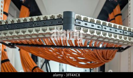 Close-up of network patch panels and organised orange data cabling inside a communications rack, showing structured cabling infrastructure used for da Stock Photo