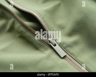 A close-up shot of a modern plastic zipper on an olive green jacket. Stock Photo