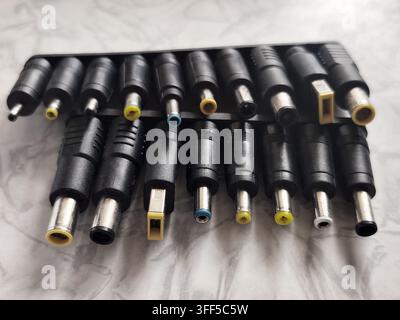 Set of various laptop power adapter tips and connectors arranged in rows on a light gray patterned surface, close up shot. Stock Photo