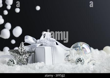 White Christmas gift with silver star and clear ornaments in snow on black background for festive New Year greeting banner Stock Photo