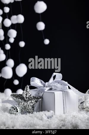 White Christmas gift with silver star in snow and falling white decorations on black background for vertical New Year greeting design Stock Photo
