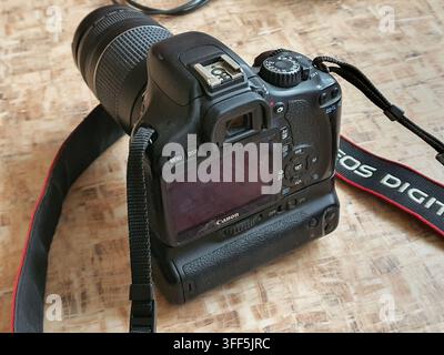 Close-up rear view of a black Canon EOS digital SLR camera with a telephoto zoom lens attached, resting on a light brown wooden or cork-patterned Stock Photo