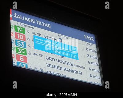A nighttime close-up view of a public transportation LED information display at Žaliasis Tiltas (Green Bridge) in Vilnius, Lithuania, showing bus and Stock Photo