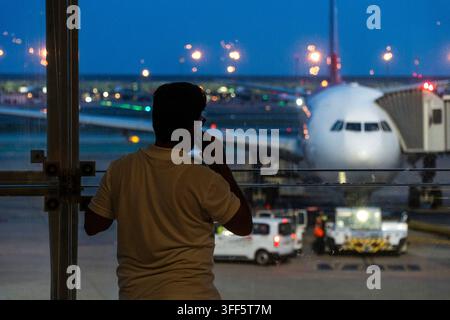 A person stands at an airport window, watching a large airplane parked on the tarmac. Stock Photo