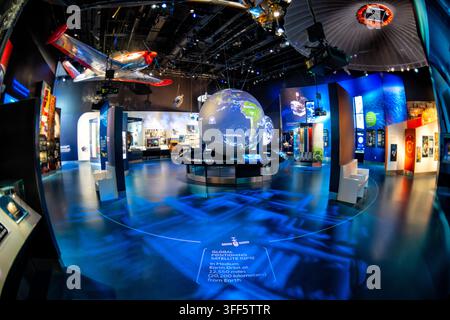 One World Connected Gallery at the Air and Space Museum | WASHINGTON D.C., United States — A rotating globe tracks orbiting satellites in the One World Connected gallery at the National Air and Space Museum, with a red racing plane suspended overhead. The floor display marks the Global Positioning System's medium Earth orbit at roughly 12,550 miles (20,200 km) above the planet, illustrating how satellite constellations underpin modern navigation. The gallery traces how aviation and spaceflight technology reshaped global communication and everyday life. Stock Photo