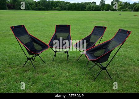 Portable mesh camping chairs with red trim standing in grassy park clearing Stock Photo