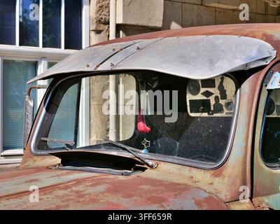 Detailed front view of an antique pickup truck cab featuring a custom metal sun visor, weathered rust-patterned paint, windshield wipers, and mini box Stock Photo