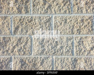 A flat view shows a wall made from beige concrete blocks. The blocks have a rough texture and are arranged in a running bond pattern. This wall appear Stock Photo